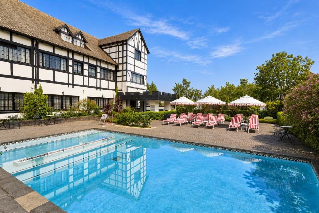 a swimming pool in front of a building with chairs and umbrellas at ANEW Hotel Hilton Pietermaritzburg in Hilton