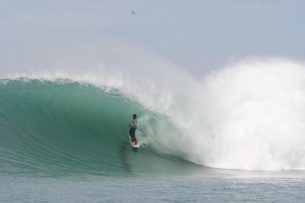 a man riding a wave on a surfboard in the ocean at Marlynto Surf Camp in Hilibotodane