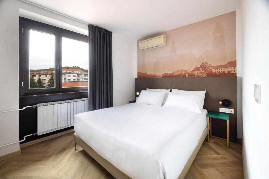 a bedroom with a white bed and a large window at B&B HOTEL Maribor Orel in Maribor