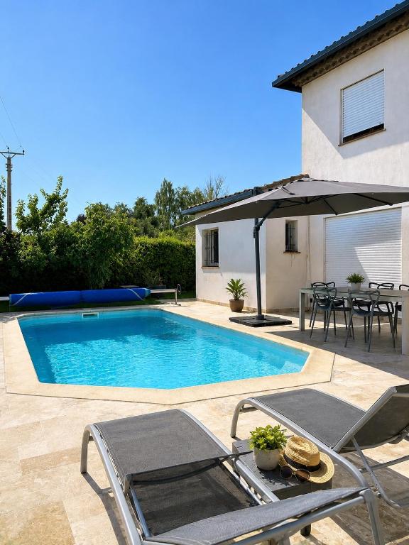 a swimming pool with a table and chairs and an umbrella at Studio neuf avec acces piscine in Valergues