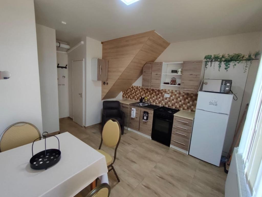 a kitchen with a white table and a white refrigerator at LŰN Apartman in Dunaföldvár