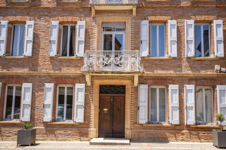 a brick building with a wooden door and a balcony at Maison Bacchus 31 in Buzet-sur-Tarn