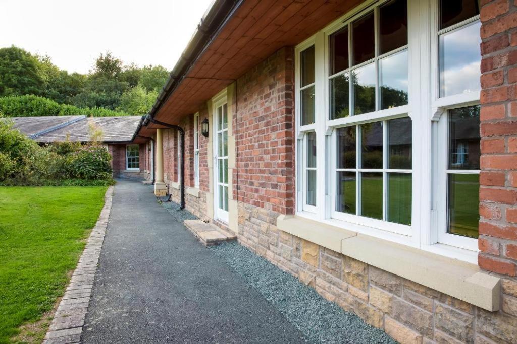 a brick building with white windows and a sidewalk at Caradoc Country Cottages in Shrewsbury