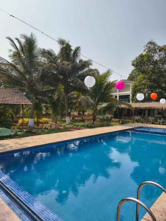 a blue swimming pool with palm trees in the background at Saiesh resort in Alibaug