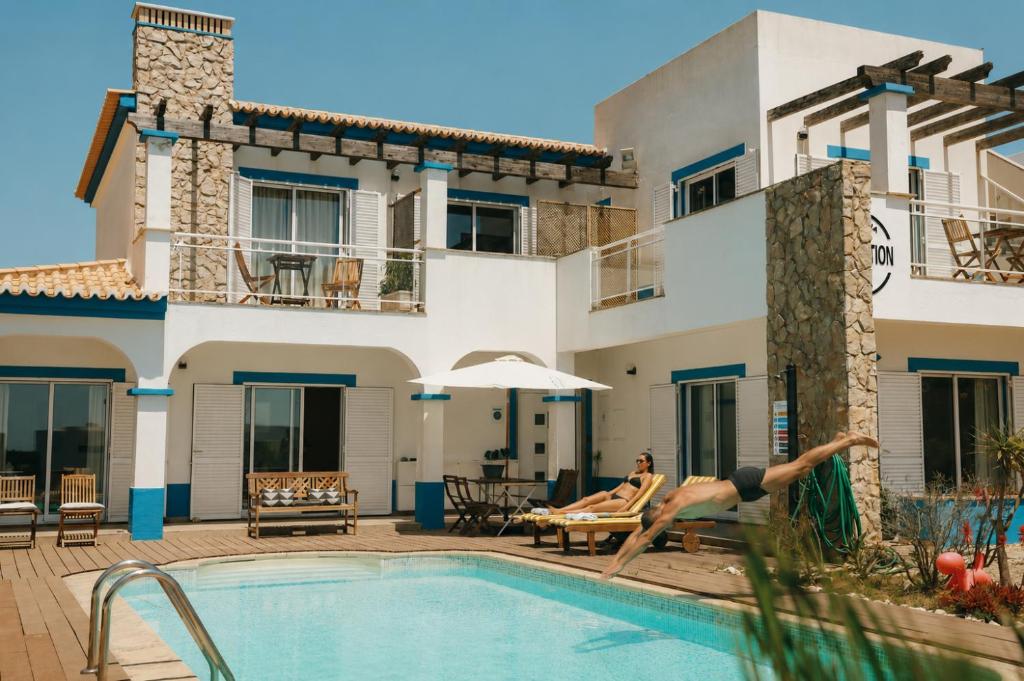 a woman diving into a swimming pool in front of a villa at Arrifana Destination Suites in Aljezur