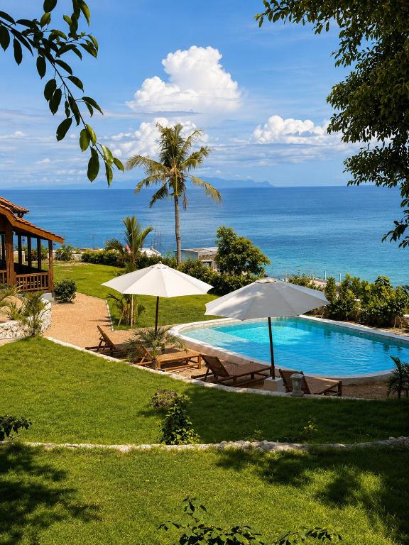 a swimming pool with two umbrellas and the ocean at 5BR, Ocean View, Private Pool, Villas Roc-Azur in Sampalan