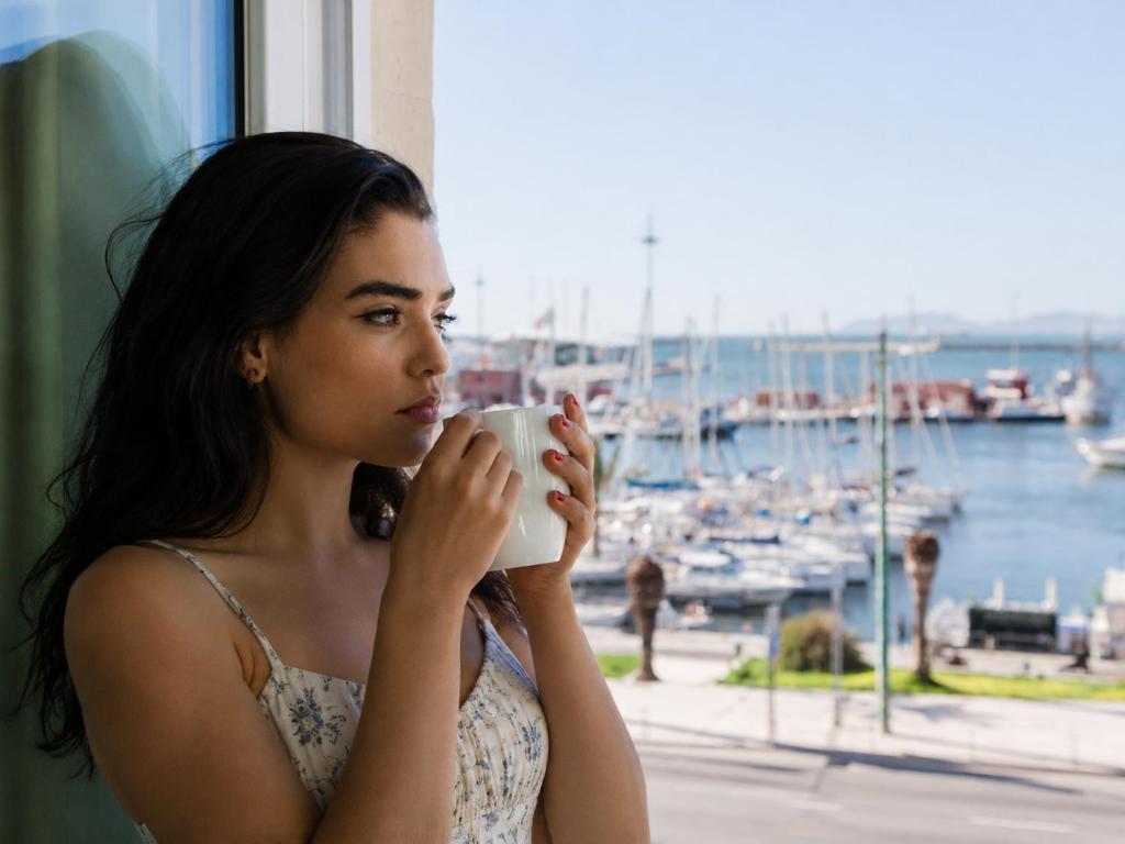a woman drinking from a coffee cup in front of a window at Hotel Aristeo in Cagliari