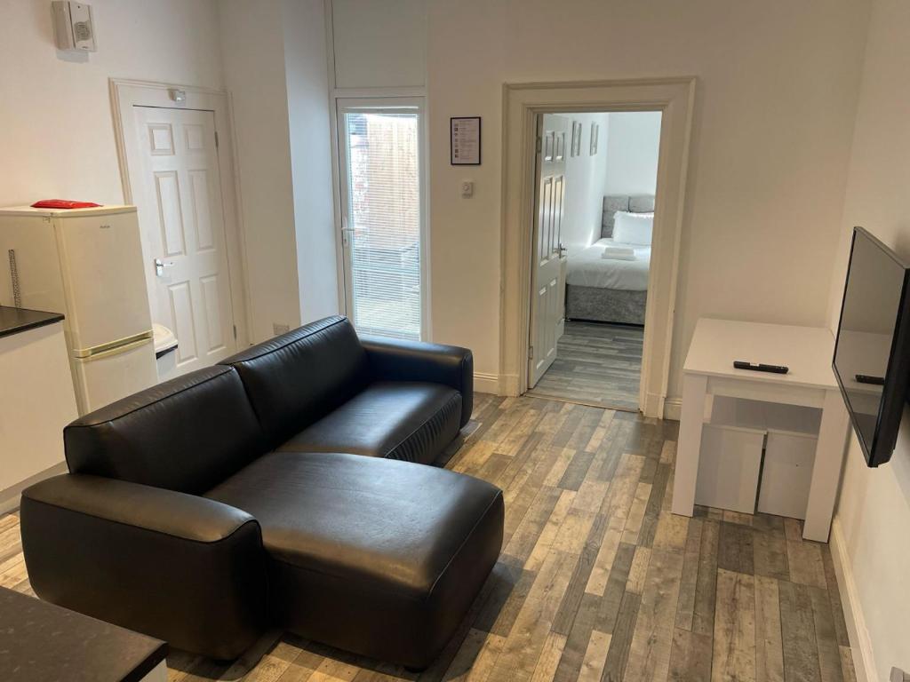 a living room with a black leather couch and a bedroom at Elder Park Apartments in Glasgow