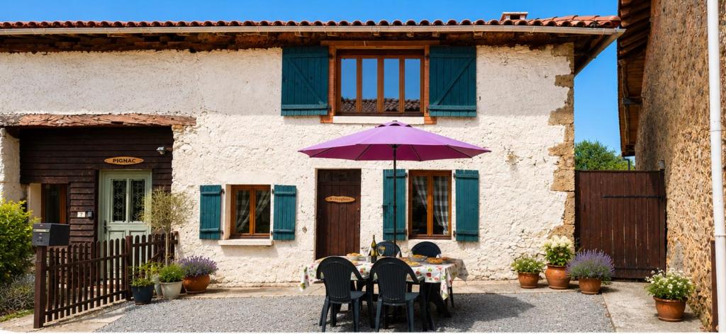 a table with a purple umbrella in front of a house at Charming Gite with pool - peaceful coumtryside in Charente in Exideuil