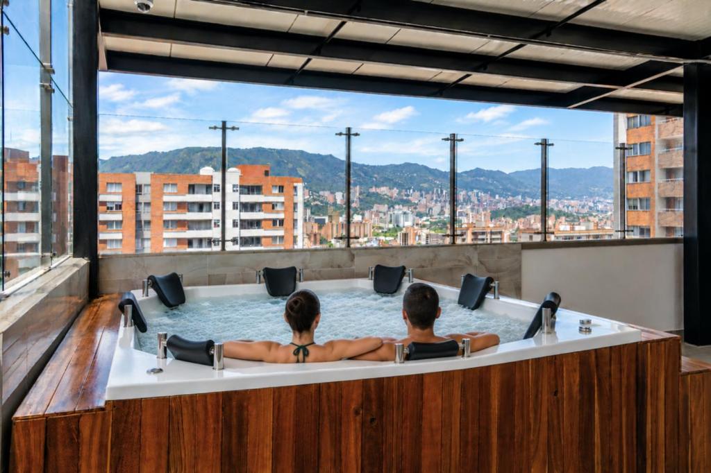two people in a bathtub with a view of a city at Hotel Colores Estadio in Medellín