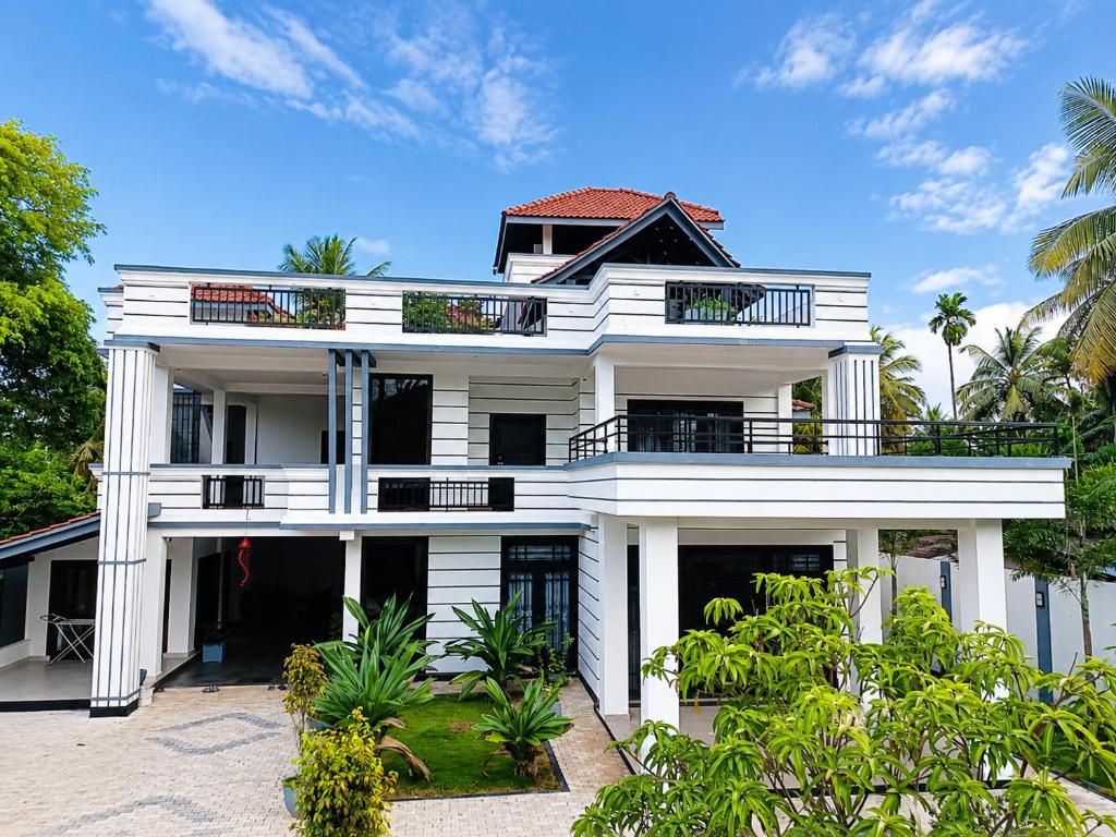 a white house with a balcony and palm trees at ANABEE HOLIDAY Inn in Jaffna