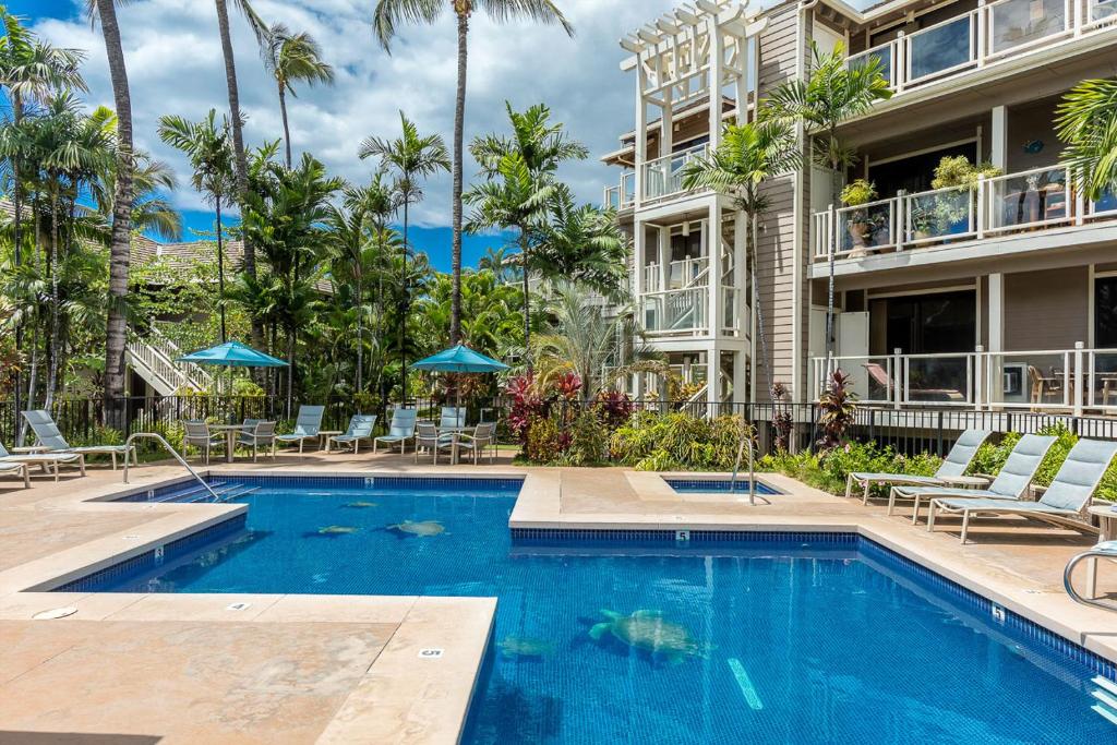 a swimming pool in front of a building with palm trees at Grand Champions 185 in Wailea