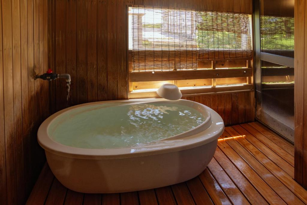 a bath tub in a wooden bathroom with a window at Kusatsu Onsen Eidaya in Kusatsu