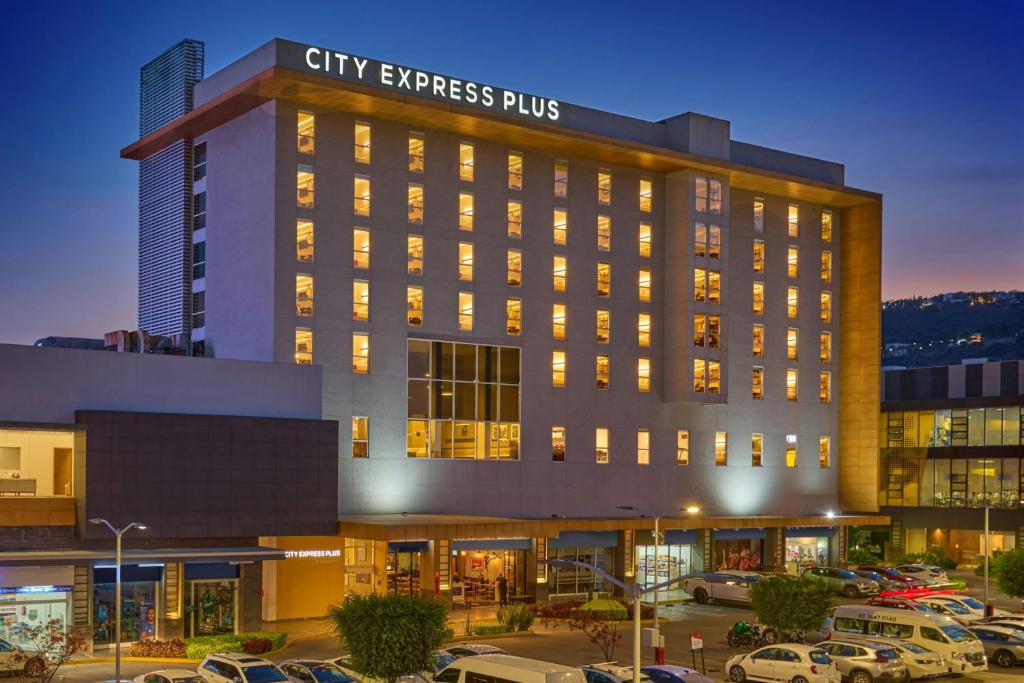 a building with cars parked in a parking lot at City Express Plus by Marriott Guadalajara Palomar in Guadalajara