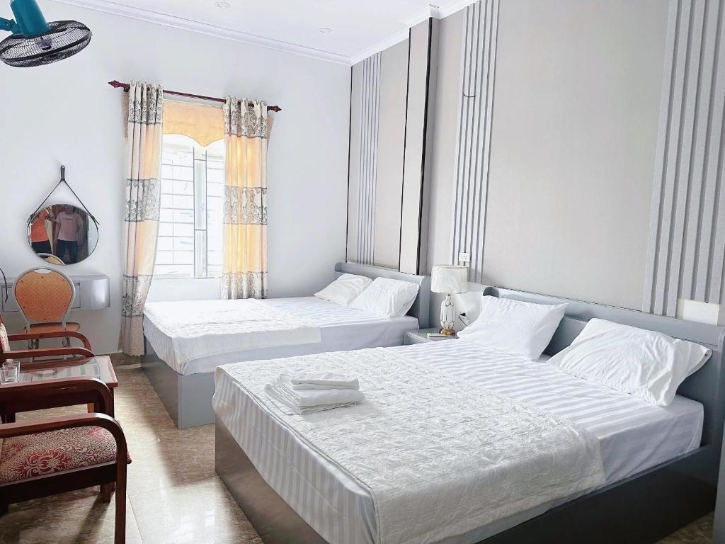 a white bedroom with two beds and a chair at Homestay Cô Tô in Đảo Cô Tô