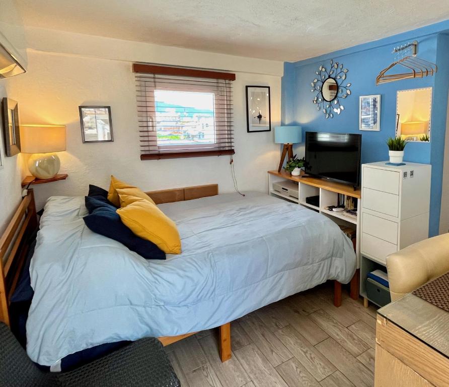 a bedroom with a bed with yellow pillows and a television at Le Petit Bonheur - Peaceful Rooftop - 3 min Beach in Puerto Vallarta