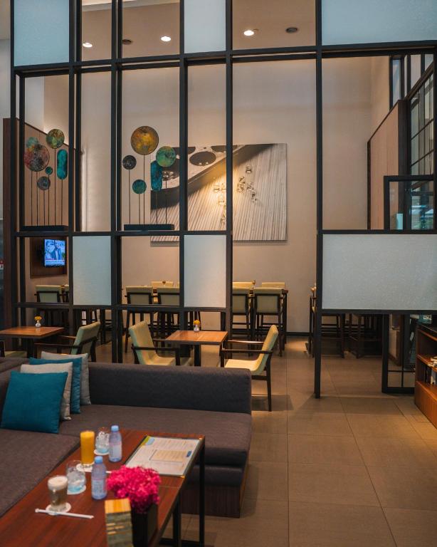 A lounge and waiting area with sofas, small tables and a glass-partitioned dining space.