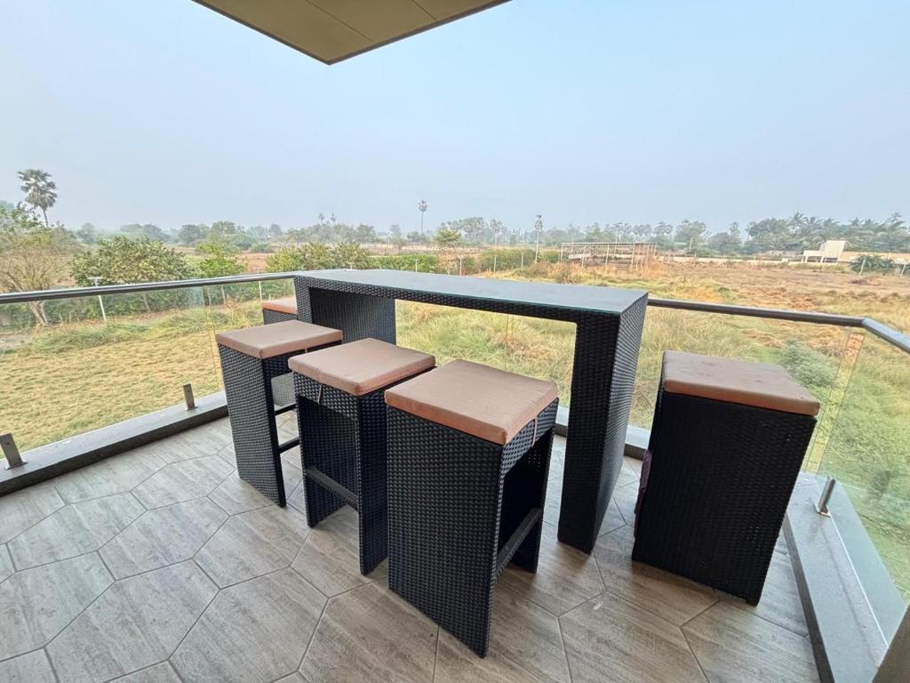 a balcony with four stools and a view of a field at Manav Farmhouse in Olpād