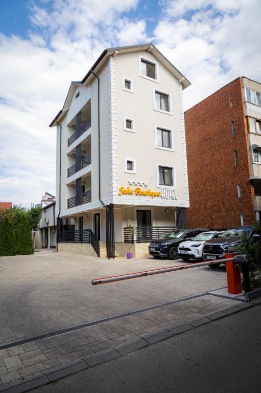 a white building with cars parked in a parking lot at Jolie Boutique Hotel in Craiova