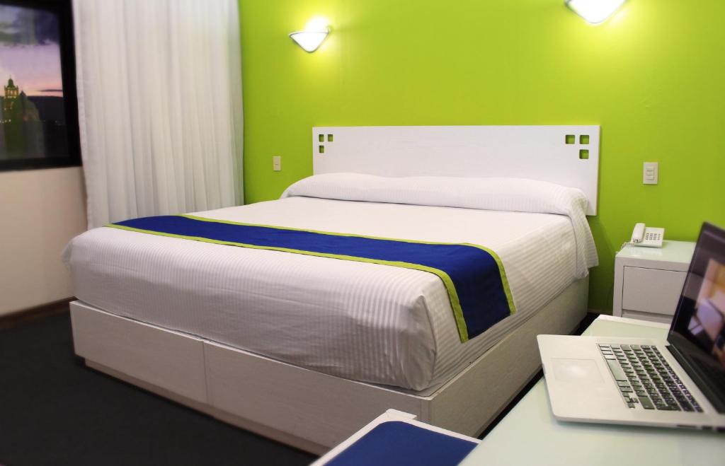 Vista Express Morelia by Arriva Hospitality Group في موريليا: غرفة نوم مع سرير وجهاز كمبيوتر محمول على مكتب