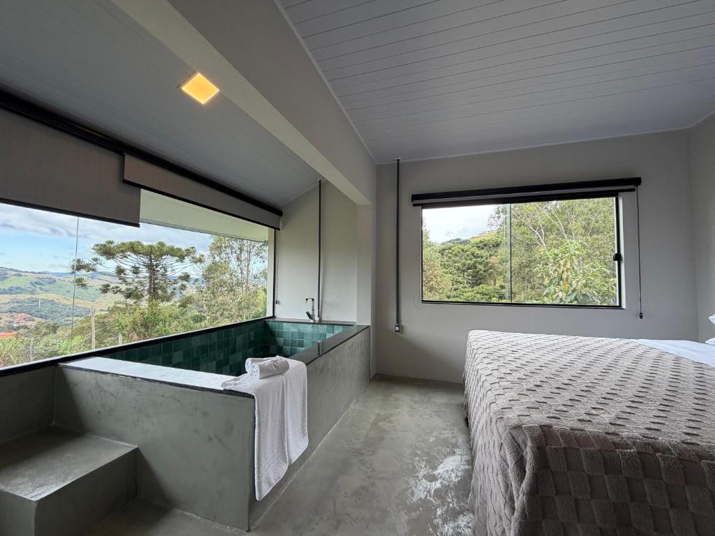 a bedroom with a tub and a bed with a large window at Refúgio Deusmideu in São Bento do Sapucaí