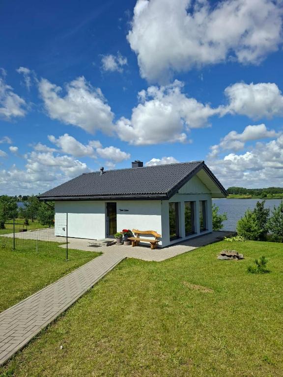 a small white house with a patio and a lake at Marių Kalvos in Palėvenėlė