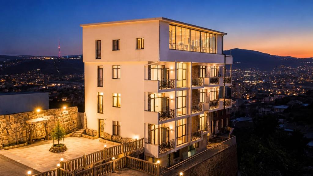 a tall white building with a balcony at night at Panorama Hills Apart-Hotel in Tbilisi City