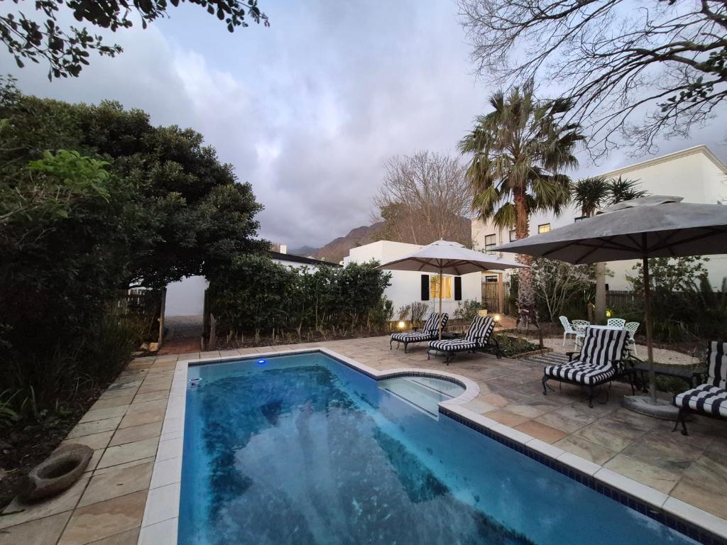 a swimming pool with chairs and umbrellas in a yard at Petit Ermitage in Franschhoek