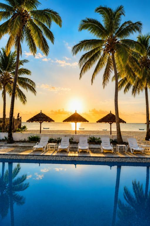 a pool at the beach with palm trees and chairs at BIANCO AZZURRO Hotel & Restaurant in Pwani Mchangani