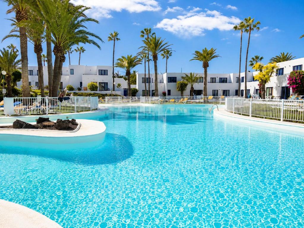 a large pool with palm trees and buildings at Los Barqueros Suites Palm in Corralejo