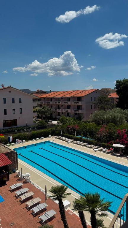a large swimming pool with chairs and a building at Green Sporting Club Hotel in Alghero
