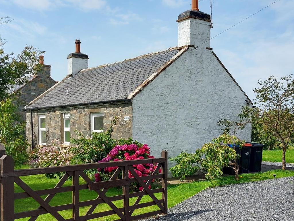 a house with a fence and flowers in front of it at Wee Dug Hoose in Glenluce