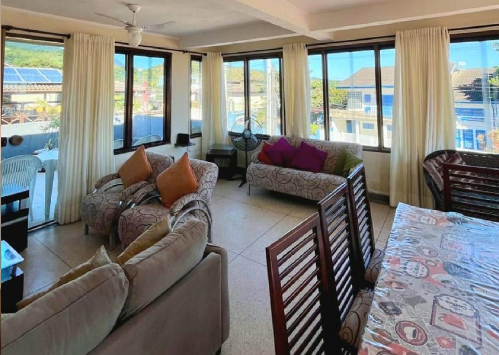 a living room with couches and chairs and windows at Apartamento Vista ao Mar Maresias in Maresias