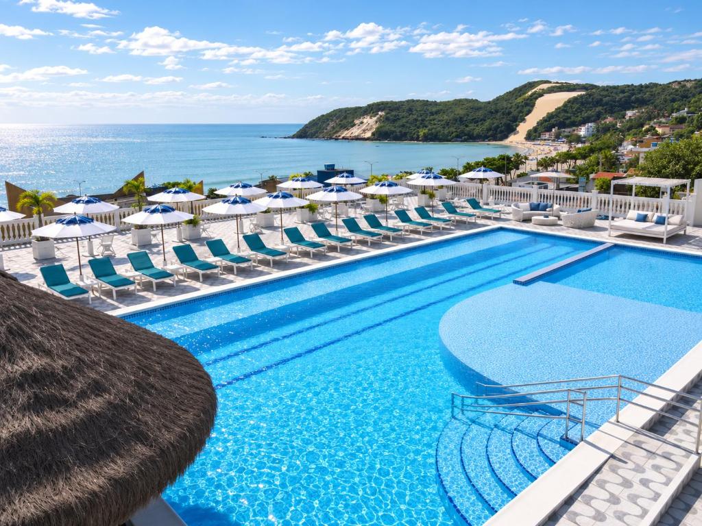 a pool with chairs and umbrellas and the ocean at SERHS Beach Hotel in Natal