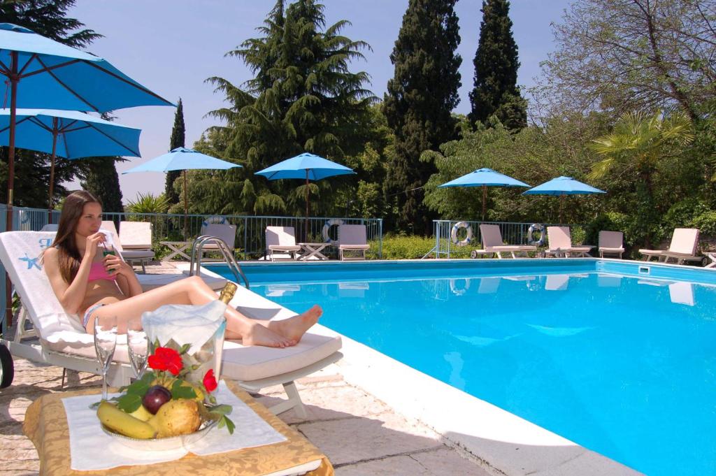 eine Frau auf einem Stuhl neben einem Pool in der Unterkunft Hotel Broglia in Sirmione