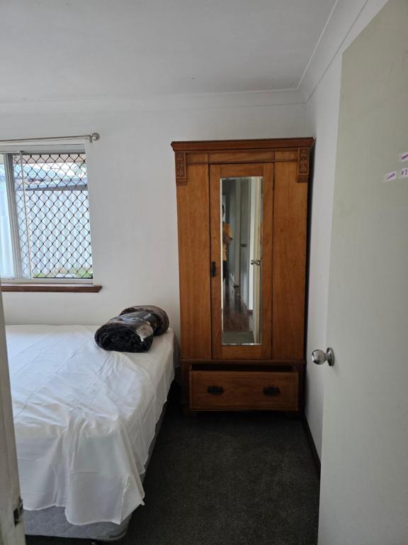 ein Schlafzimmer mit einem Bett und einem Holzschrank in der Unterkunft Wattle Close - Room in a Shared house in Kelmscott