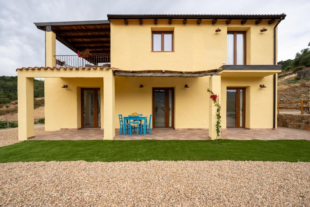 a yellow house with a table and blue chairs at Agriturismo Cirra in Tertenìa
