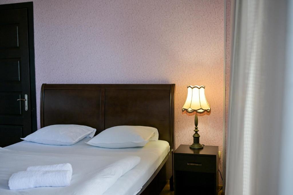 a bed with two pillows and a lamp on a table at Kutaisi Grand Suites in Kutaisi