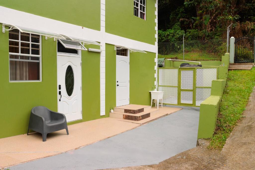 a green house with a black chair on a patio at Middleham Forest Nook in Roseau