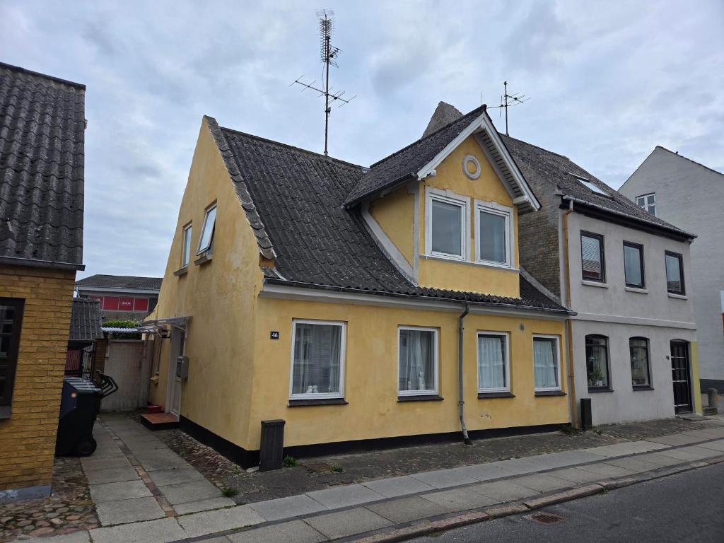 a yellow house with a black roof on a street at Holiday Hus in Rudkøbing