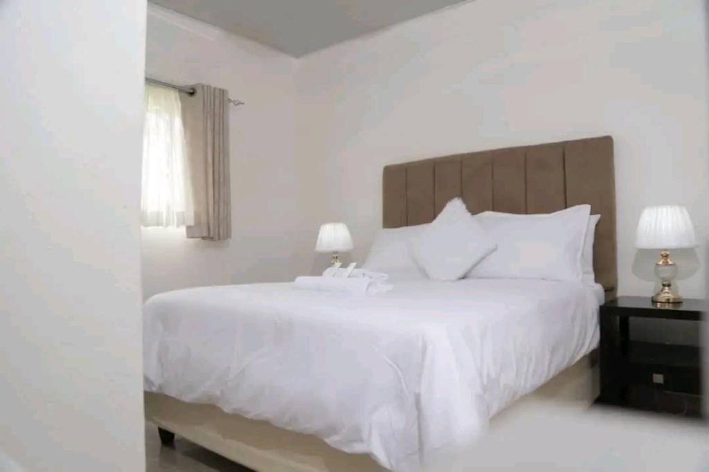 a white bedroom with a large white bed and a window at Dopiro Lodge and Gardens in Nyanda
