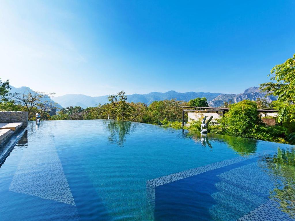 a pool of blue water with mountains in the background at Botanica Khao Yai by Scenical in Mu Si