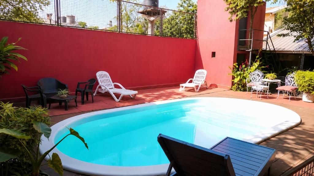 a swimming pool with chairs and a red wall at JM Resort Iguazu in Puerto Iguazú