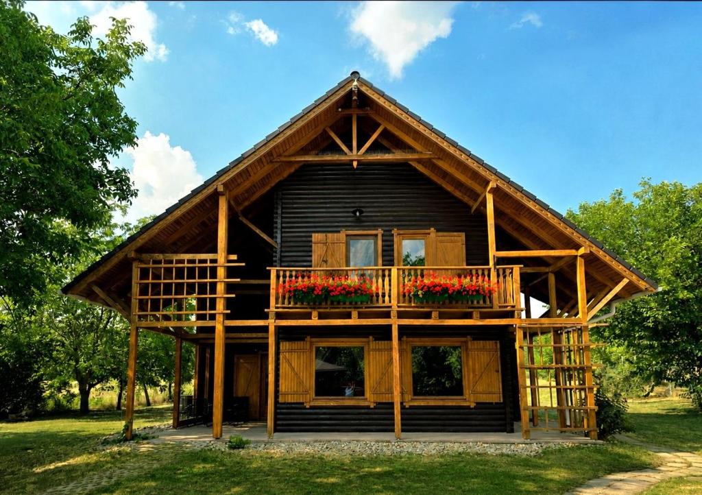 a log cabin with a balcony and flowers on it at Komondor Vendégház in Vácrátót