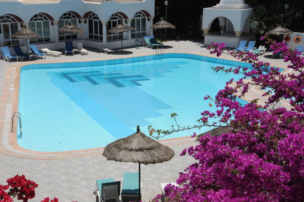 una piscina con sillas, sombrilla y flores púrpuras en Hotel Menara en Hammamet