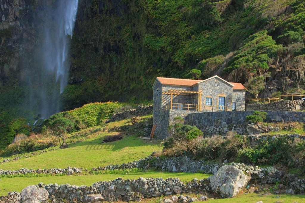 ein Haus auf einem Hügel mit einem Wasserfall im Hintergrund in der Unterkunft Moinho da Cascata in Faja Grande