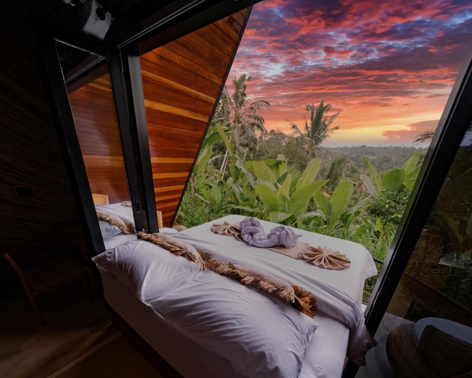a bed in a room with a view of a sunset at Delta Casa Ubud - A-Frame Jungle Retreat with Volcano View and Hot-Tubs in Gianyar