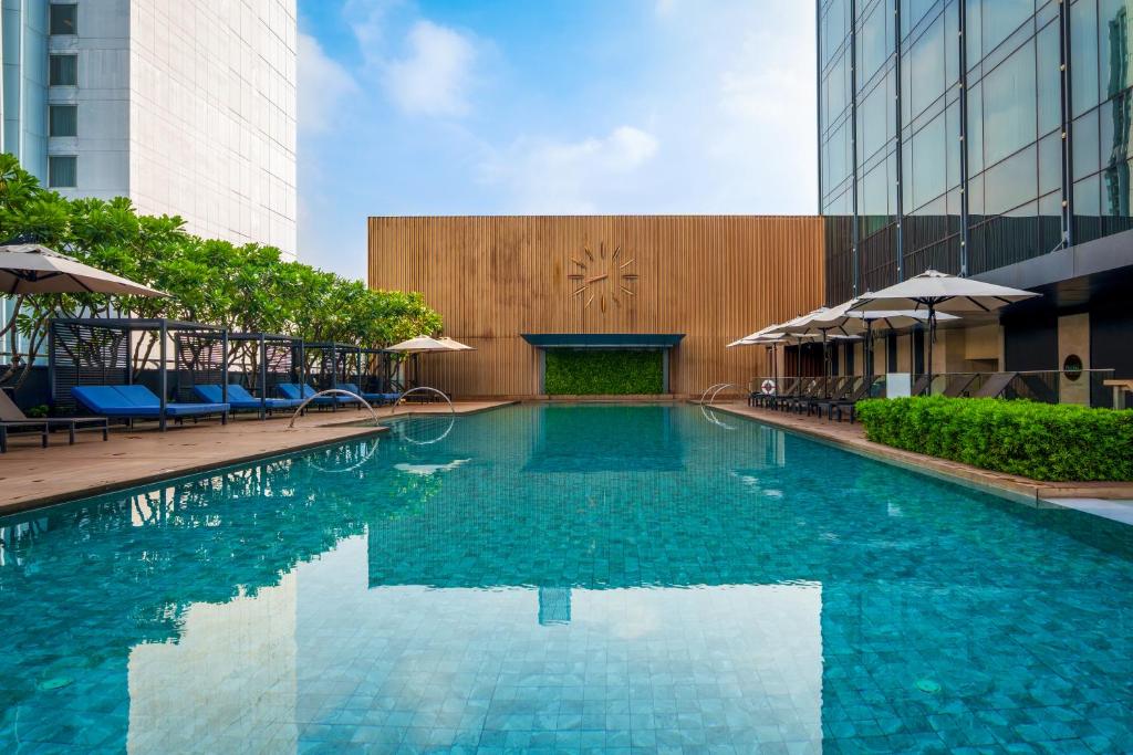 a swimming pool with chairs and umbrellas in a building at Carlton Hotel Bangkok Sukhumvit in Bangkok