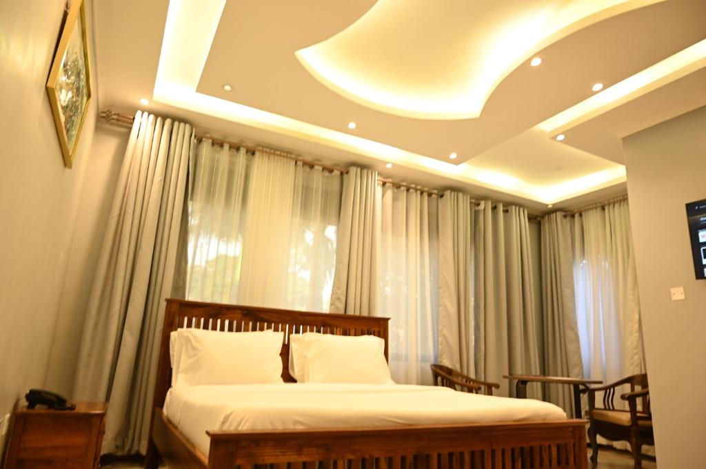 a bedroom with a bed with white sheets and curtains at Neon Hotel in Kampala