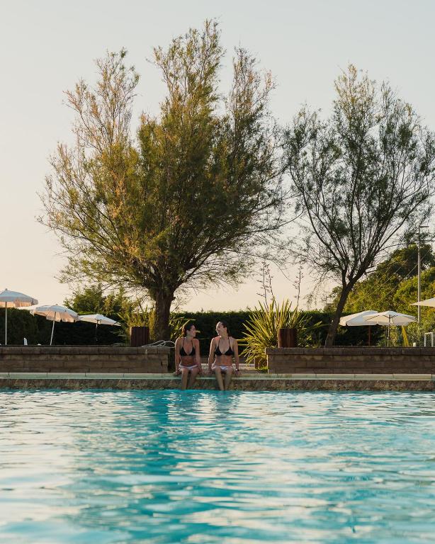 two women in bathing suits sitting next to a swimming pool at Agriturismo Le Pescine in Vada